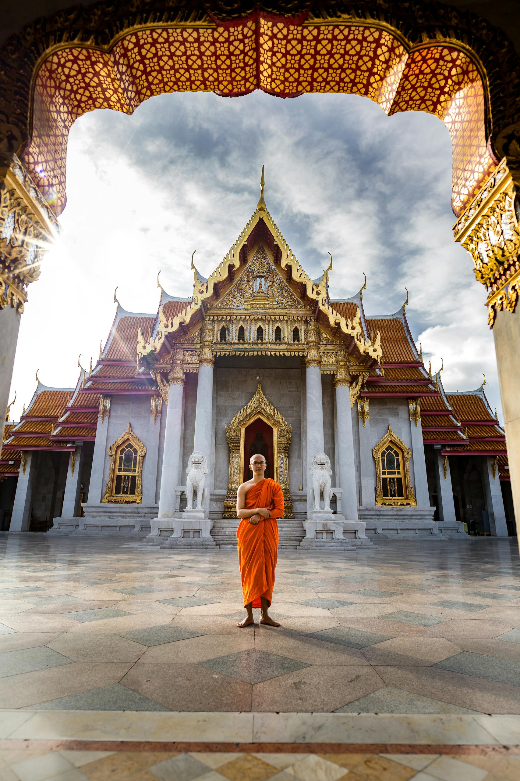 A Buddhist monk standing in front of the iconic Wat Benchamabophit Temple, Bangkok, capturing spiritual tranquility.