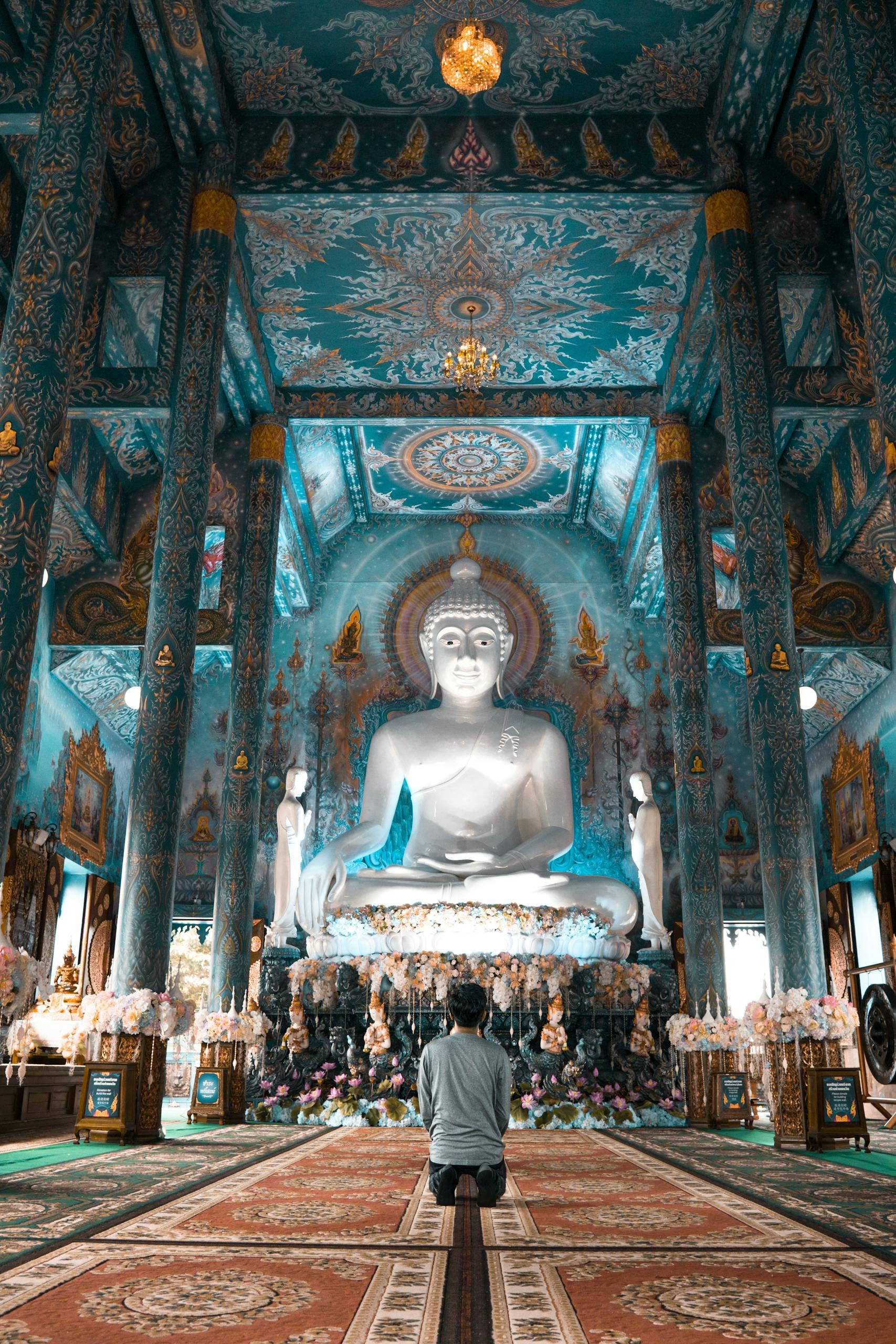 A serene view of a person worshipping inside the ornate Blue Temple of Chiang Rai, Thailand.