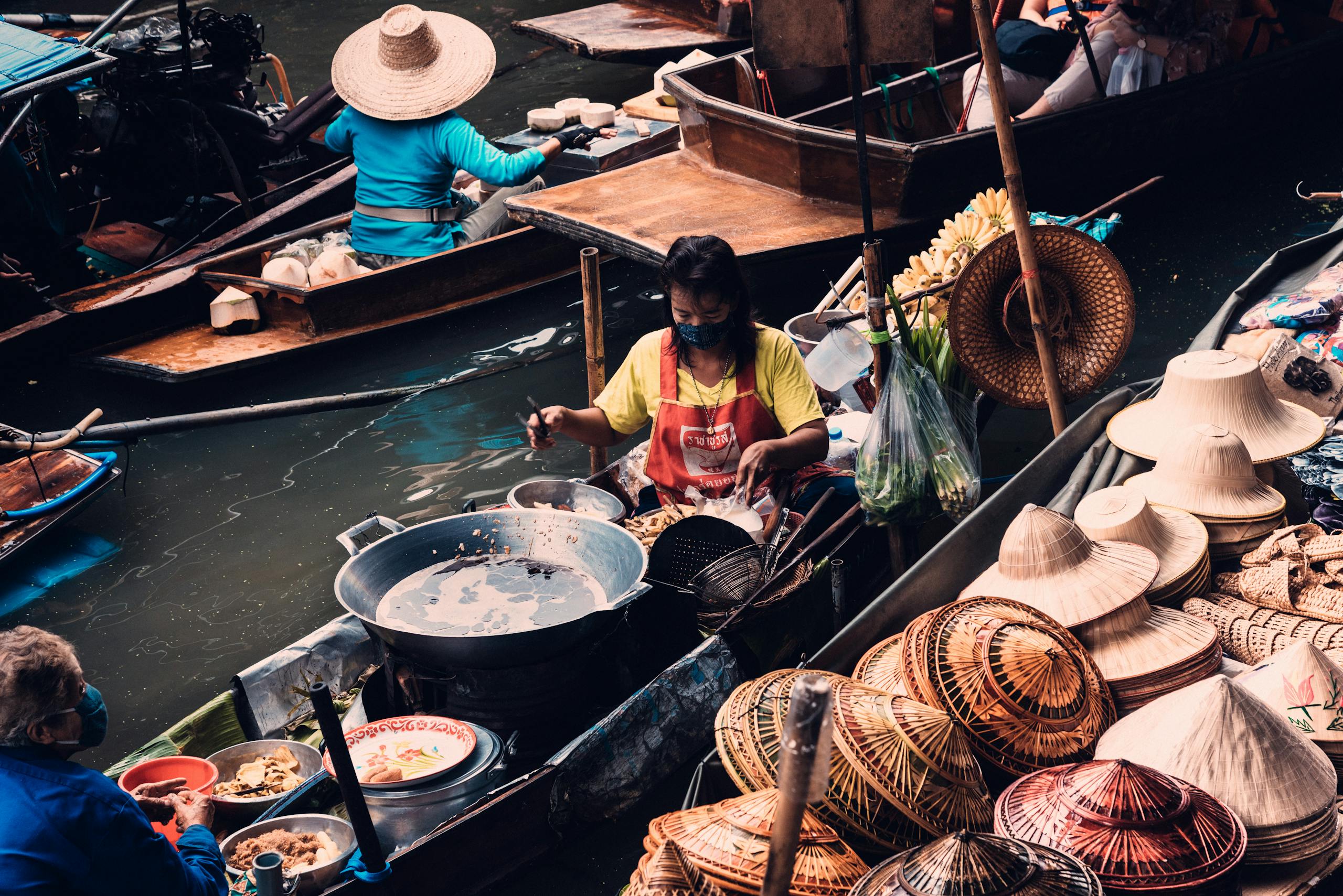 Traditional floating market in Bangkok featuring vendors selling hats and food from boats.